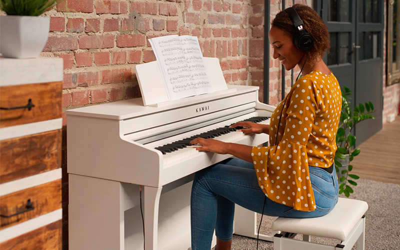 Digitální piano KAWAI CA49W Žena se sluchátky hrající na KAWAI CA49W